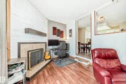 Living area featuring wood-finish flooring, a fireplace with a tile surround and dark mantel, and white plank-style wall paneling - 
