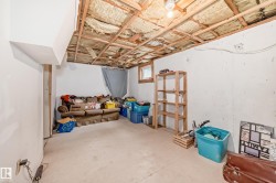 Unfinished basement area featuring exposed ceiling joists and insulation, a small window with wood trim, and painted concrete walls - 