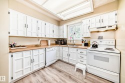 Kitchen featuring extensive white cabinetry with black hardware, wood-finish countertops, and wood-finish flooring - 