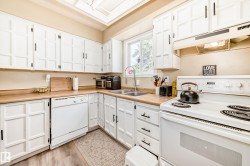 Bright kitchen featuring white cabinetry with black hardware, wood-finish countertops, and a double basin stainless steel sink with a window above - 