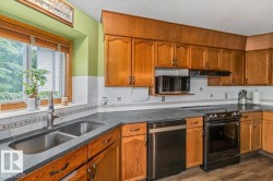 Kitchen featuring wood cabinetry, dark countertops, a stainless steel double basin sink, and a four-burner electric range with a microwave above - 