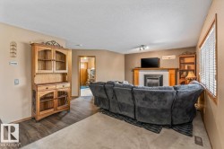 Living area featuring a fireplace with a stone surround and wood mantle, wood-finish flooring, track lighting, and a window with blinds - 