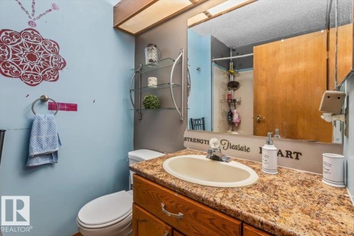 Bathroom featuring a vanity with an oval sink and a granite-look countertop, wood-finish cabinetry with silver hardware, a wall-mounted mirror, and a toilet - 16 Harrold Place, St. Albert, AB - Indoor Photo Showing Bathroom