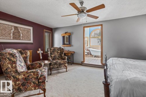 Spacious room featuring carpeting, a ceiling fan, and direct access to a bathroom with a visible clawfoot tub and arched window - 16 Harrold Place, St. Albert, AB - Indoor Photo Showing Bedroom
