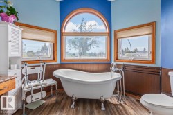 Clawfoot tub with chrome fixtures, wood-finish flooring, and a large arched window - 
