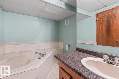 Bathroom featuring a built-in jetted tub, white tile surround, a vanity with a dark speckled countertop, and an integrated white sink - 16 Harrold Place, St. Albert, AB - Indoor Photo Showing Bathroom
