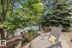 Private outdoor space featuring a stone patio, a multi-level garden bed with retaining walls, and mature trees providing natural screening - 