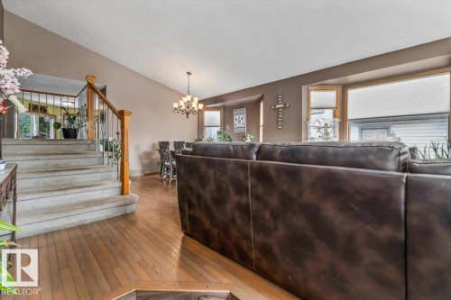 Open concept living space featuring wood-finish flooring throughout, a carpeted staircase with wood handrails and metal balusters, and a dining area with a chandelier and bay window - 16 Harrold Place, St. Albert, AB - Indoor Photo Showing Living Room