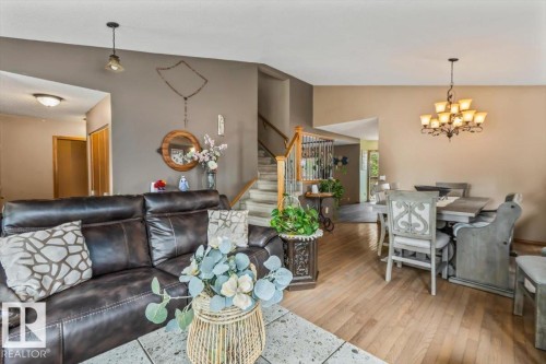 Open-concept living and dining areas featuring light wood-finish flooring, a contemporary chandelier, and a prominent staircase with wood banister and metal spindles - 16 Harrold Place, St. Albert, AB - Indoor Photo Showing Living Room