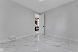 Spacious room featuring large format marble-look tile flooring, crisp white baseboards, light grey wall paint, and a modern white door with black hardware - 