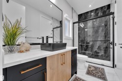 Contemporary bathroom featuring a black vessel sink, black faucets, a white countertop, and two-tone cabinetry with black and wood-finish doors - 