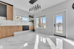 Modern space featuring a striking linear chandelier, wood-finish and black cabinetry, white countertops, geometric tile backsplash, and oversized marble-look floor tiles - 