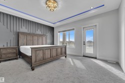 Modern bedroom featuring a textured accent wall, recessed ceiling with blue ambient lighting, and a contemporary chandelier - 
