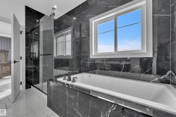 Soaking tub with sleek black stone surround and matte black fixtures, set against matching stone walls - 