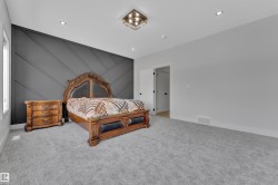 Feature wall with geometric paneling, recessed lighting, central ceiling light fixture, window with white trim, and gray carpet - 