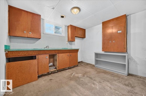Utility room featuring a built-in sink, wood-finish cabinetry, a drop ceiling, a window, and open shelving - 12134 42 Street Nw, Edmonton, AB - Indoor Photo Showing Other Room