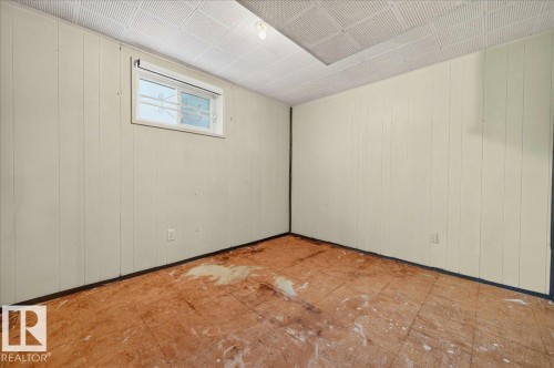 Interior space featuring painted vertical paneling, a single window with security bars, and a drop ceiling with a recessed light fixture - 12134 42 Street Nw, Edmonton, AB - Indoor Photo Showing Other Room
