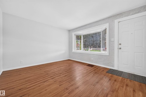 Spacious room featuring wood-finish flooring, a white bay window, a multi-panel entry door, and light-toned walls - 12134 42 Street Nw, Edmonton, AB - Indoor Photo Showing Other Room