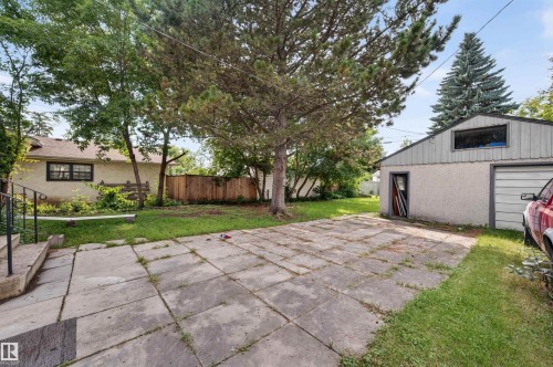 Spacious backyard featuring a large paved patio area, mature trees, and a detached two-car garage with a stucco finish - 12134 42 Street Nw, Edmonton, AB - Outdoor