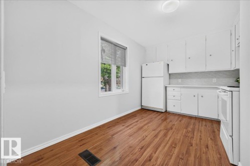 Kitchen area featuring wood-finish flooring, white cabinetry, a window with blinds, white appliances, and a flush mount ceiling light - 12134 42 Street Nw, Edmonton, AB - Indoor Photo Showing Kitchen