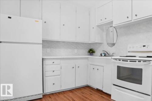 Kitchen featuring wood-finish flooring, white cabinetry, a corner sink, and a white range - 12134 42 Street Nw, Edmonton, AB - Indoor Photo Showing Kitchen