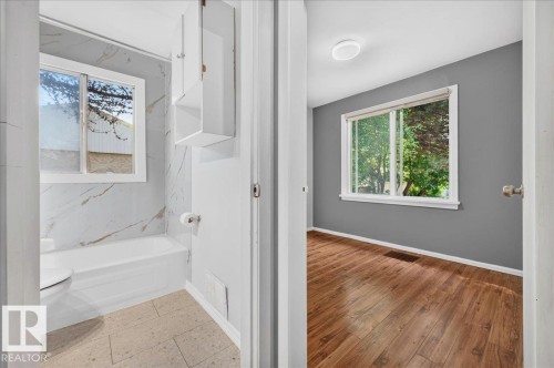 Bathroom featuring a white bathtub with marble-look surround, a window, and wall-mounted storage cabinetry - 12134 42 Street Nw, Edmonton, AB - Indoor