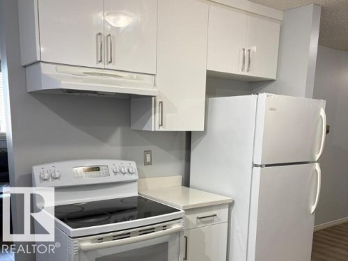 Kitchen featuring white cabinetry with silver-tone hardware, a matching white electric range with a black cooktop, a white refrigerator, and light-toned countertops - #103 10023 164St St Nw, Edmonton, AB - Indoor Photo Showing Kitchen