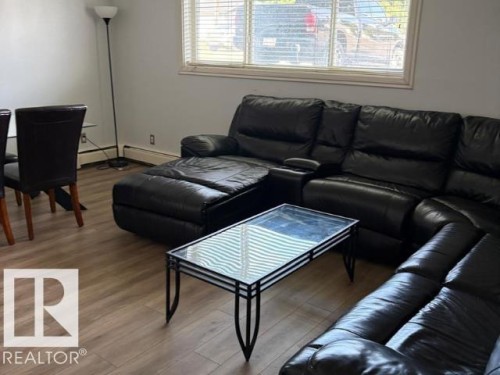 Interior space featuring wood-finish flooring, neutral wall paint, and a large window with blinds - #103 10023 164St St Nw, Edmonton, AB - Indoor Photo Showing Living Room