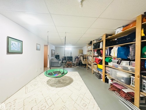 Finished basement featuring drop ceiling, painted concrete flooring, and built-in wood shelving for extensive storage - 221 Parkview Drive, Wetaskiwin, AB - Indoor
