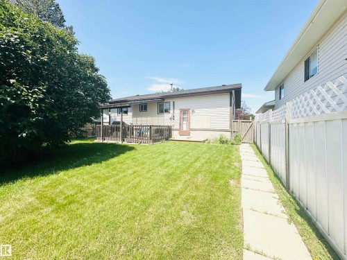 Expansive backyard featuring a large green lawn, a multi-level wooden deck, mature perimeter tree, and a concrete pathway leading to a wooden gate - 221 Parkview Drive, Wetaskiwin, AB - Outdoor With Deck Patio Veranda