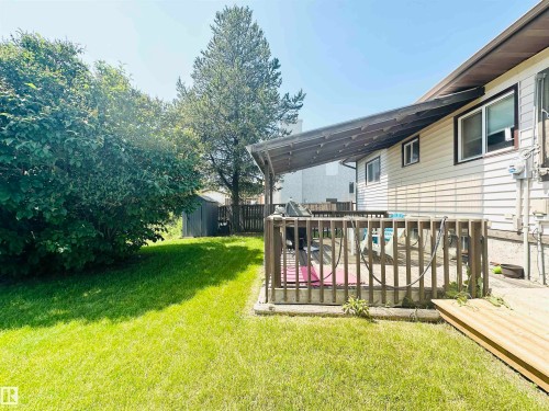 Expansive backyard featuring a covered wood-finish deck, verdant lawn, mature trees, and a storage shed - 221 Parkview Drive, Wetaskiwin, AB - Outdoor With Deck Patio Veranda