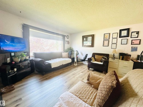 Living area featuring wood-finish flooring, a large window with roller shades, and a textured ceiling - 221 Parkview Drive, Wetaskiwin, AB - Indoor Photo Showing Living Room