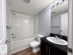 Bathroom featuring a white subway tile shower surround, a built-in tub with chrome fixtures, a dark wood-finish vanity with an integrated sink, a black countertop, and warm-toned floor tiles - 