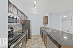 Galley kitchen featuring wood-finish cabinetry, stainless steel appliances, dark countertops, and track lighting - 