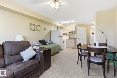 Combined living and dining area featuring carpet flooring, a ceiling fan with integrated lighting, and a compact kitchen - #230 8802 Southfort Dr, Fort Saskatchewan, AB - Indoor