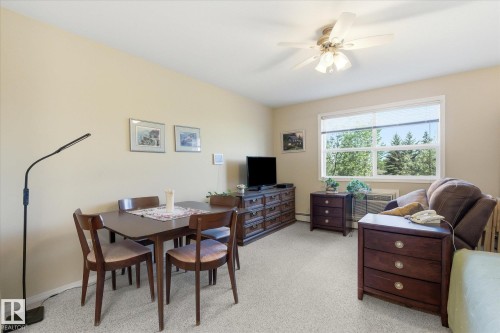Living area featuring light-toned walls, a window with exterior tree views, and a ceiling fan - #230 8802 Southfort Dr, Fort Saskatchewan, AB - Indoor