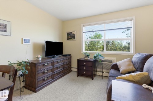 Spacious room with light-toned walls, a large multi-pane window, and neutral carpet flooring - #230 8802 Southfort Dr, Fort Saskatchewan, AB - Indoor