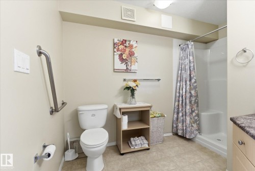 Full bathroom featuring a walk-in shower with a white surround, neutral-toned floor tiling, and a toilet - #230 8802 Southfort Dr, Fort Saskatchewan, AB - Indoor Photo Showing Bathroom
