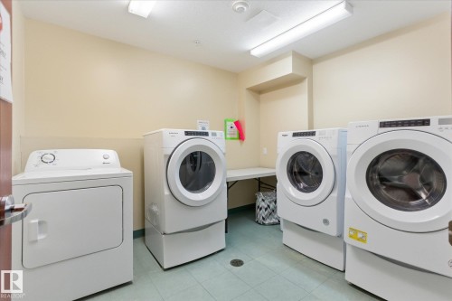 Dedicated laundry area featuring multiple front-load washers and dryers, light-colored walls, and durable flooring - #230 8802 Southfort Dr, Fort Saskatchewan, AB - Indoor Photo Showing Laundry Room