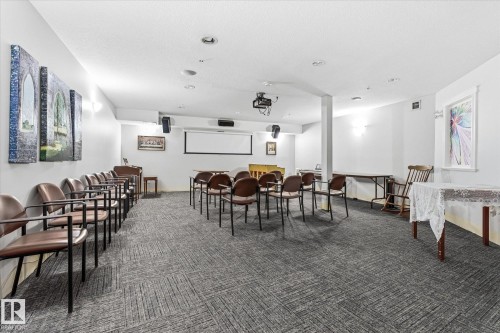 Spacious room featuring patterned carpet flooring, recessed lighting, and a prominent projection screen - #230 8802 Southfort Dr, Fort Saskatchewan, AB - Indoor Photo Showing Other Room
