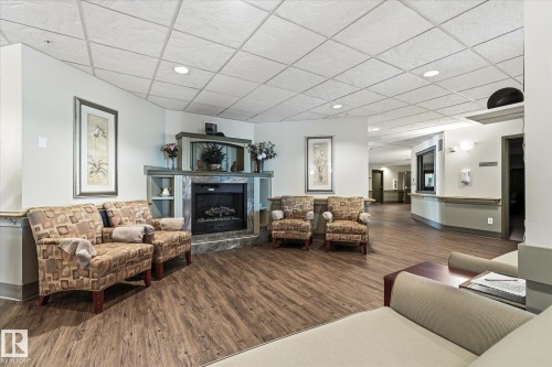 Lobby area featuring a gas fireplace with stone surround, wood-finish flooring, and recessed lighting - #230 8802 Southfort Dr, Fort Saskatchewan, AB - Indoor Photo Showing Living Room With Fireplace