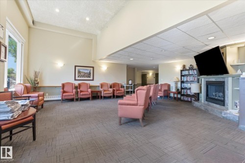 Spacious common area featuring vaulted ceilings, large windows, wall sconces, a built-in fireplace with a stone surround, and an integrated entertainment center with shelving - #230 8802 Southfort Dr, Fort Saskatchewan, AB - Indoor With Fireplace