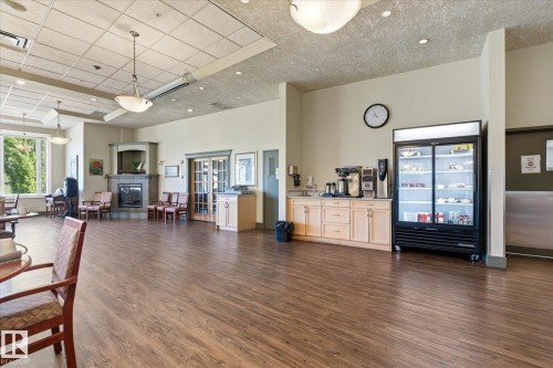 Spacious common area featuring wood-finish flooring, a built-in stone fireplace, large windows, and recessed lighting - #230 8802 Southfort Dr, Fort Saskatchewan, AB - Indoor