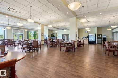 Spacious dining area featuring wood-finish flooring, numerous overhead light fixtures, and expansive windows - #230 8802 Southfort Dr, Fort Saskatchewan, AB - Indoor Photo Showing Dining Room