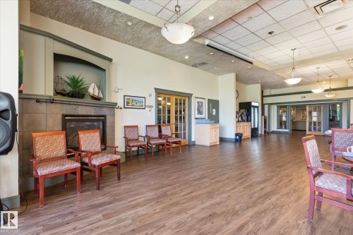 Spacious common area featuring wood-finish flooring and a tiled fireplace with an integrated mantel - #230 8802 Southfort Dr, Fort Saskatchewan, AB - Indoor