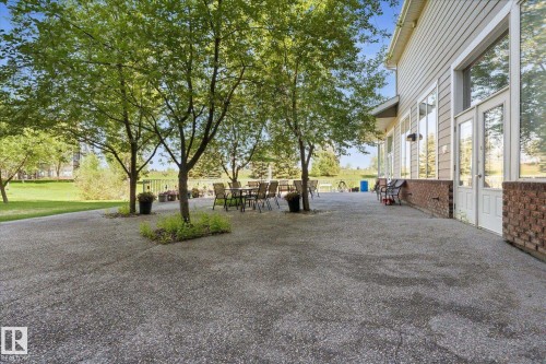 Expansive exposed aggregate patio featuring mature trees, a brick facade foundation, siding exterior, and multiple glass-paned doors - #230 8802 Southfort Dr, Fort Saskatchewan, AB - Outdoor