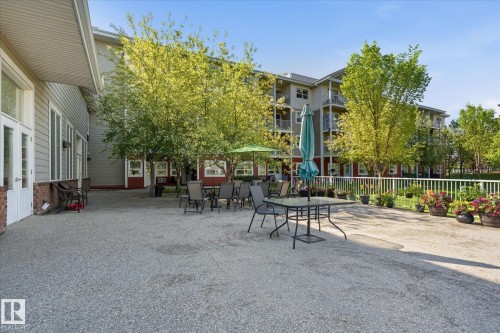 Spacious outdoor patio area featuring a textured ground surface, bordered by a white railing - #230 8802 Southfort Dr, Fort Saskatchewan, AB - Outdoor