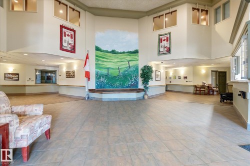 Spacious interior lobby featuring high ceilings, light-toned tiled flooring, and a large wall mural - #230 8802 Southfort Dr, Fort Saskatchewan, AB - Indoor