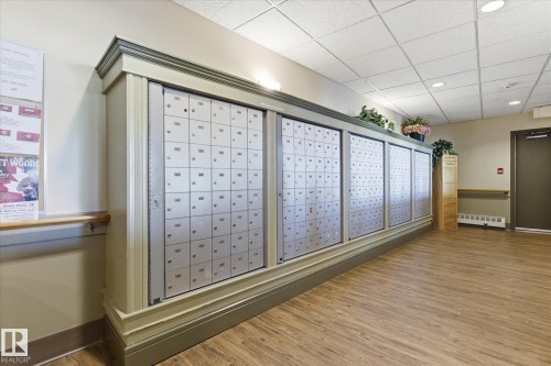 Centralized mailboxes with decorative wood trim, wood-finish flooring, recessed lighting, and a neutral wall color - #230 8802 Southfort Dr, Fort Saskatchewan, AB - Indoor Photo Showing Other Room