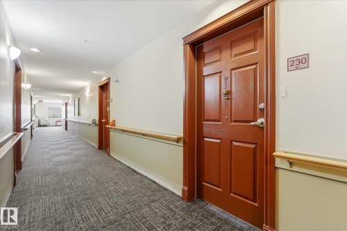 Interior hallway featuring a patterned carpet, light beige walls, and wood-finish doors - #230 8802 Southfort Dr, Fort Saskatchewan, AB - Indoor Photo Showing Other Room
